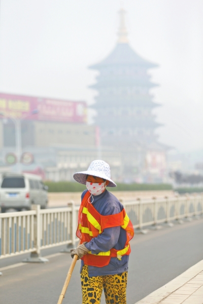 近日，在古都洛陽，環(huán)衛(wèi)工人身后的“天堂”被霧霾籠罩著。