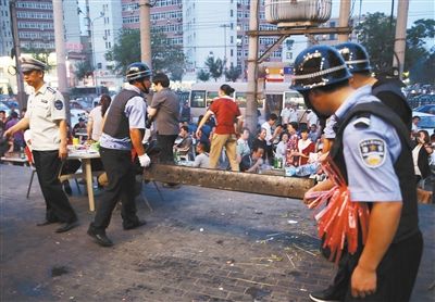 6月13日晚8點，朝陽路和青年路交叉口西側(cè)，一次聯(lián)合執(zhí)法行動中，輔警與協(xié)管抬走商戶的燒烤用具。新京報記者 尹亞飛 攝