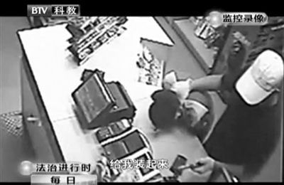 戴帽男子一手掐住加油站營業(yè)員，一手持發(fā)令槍指向另一營業(yè)員，要求“把錢給我裝起來”。