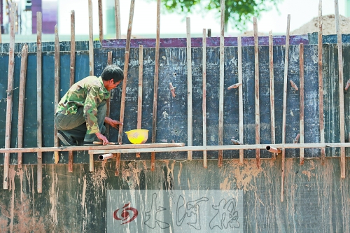 　　烈日下，狹窄的架子上，工人正用錘子固定樁基。