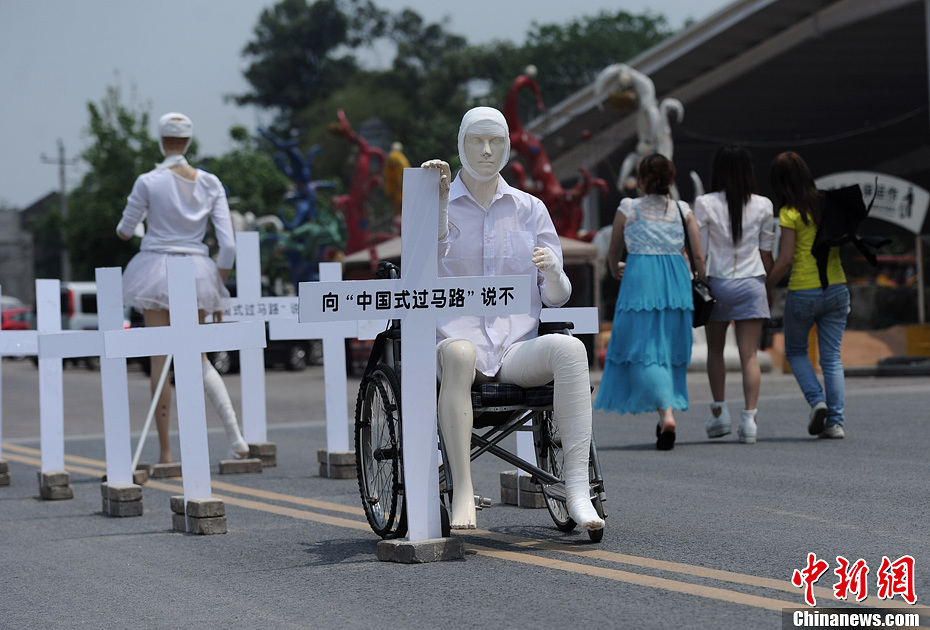 4月16日，重慶市洋人街上擺放著兩個(gè)受了傷的塑料人像“模特”，旁邊十字架上寫(xiě)著向“中國(guó)式過(guò)馬路”說(shuō)不
