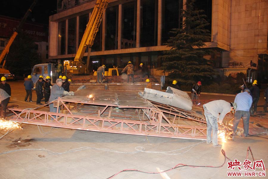 地面上的20多名工人對吊裝下的廣告牌進行分割。