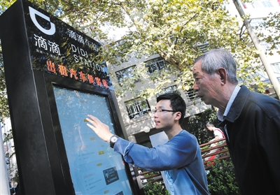 10月15日，滴滴工作人員（左）指導乘客使用“滴滴車站”的電子屏預約出租車。