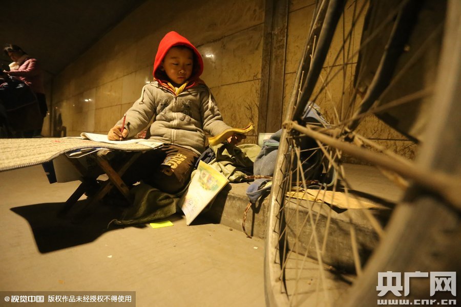 2015年11月8日晚，鄭州，7歲男孩涵洞橋下陪父母練攤，路邊燈下坐小馬扎上寫作業(yè)。