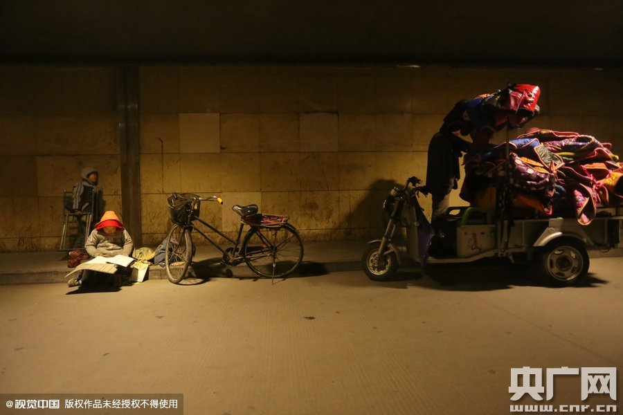 2015年11月8日晚，鄭州，7歲男孩涵洞橋下陪父母練攤，路邊燈下坐小馬扎上寫作業(yè)。