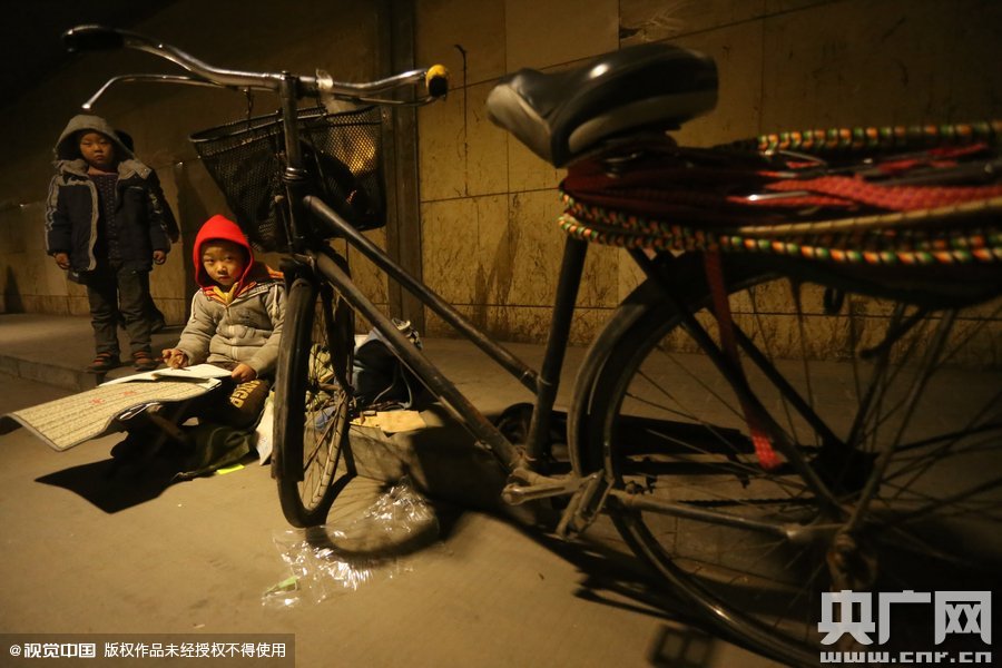 2015年11月8日晚，鄭州，7歲男孩涵洞橋下陪父母練攤，路邊燈下坐小馬扎上寫作業(yè)。
