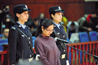 被告人盧梅低著頭，站在朝陽法院刑事審判庭的被告席上。