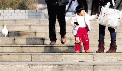 昨天中午，一女孩拉著家長(zhǎng)的手在紫荊山公園曬太陽(yáng)，氣溫升高，孩子的棉衣解開了扣子。