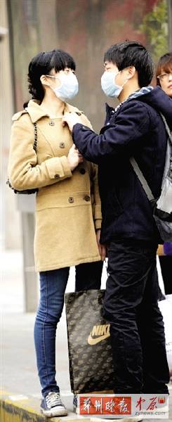 公交站臺(tái)上，一對(duì)年輕人戴著口罩，系緊衣領(lǐng)。